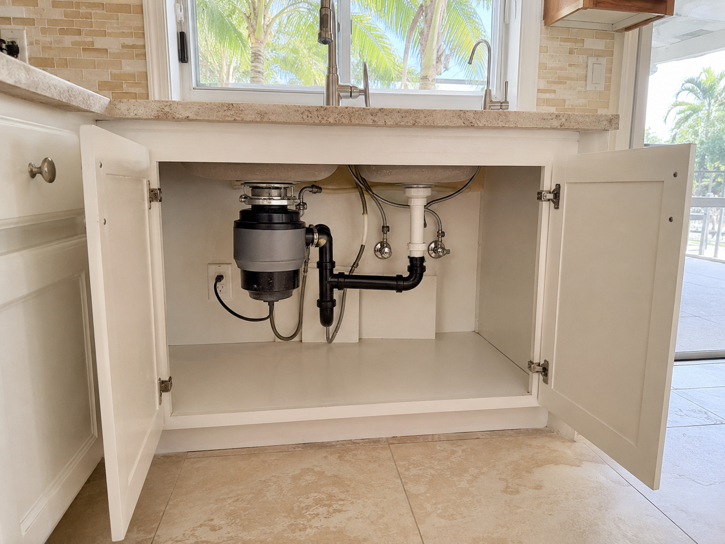 Garbage disposal installation beneath a kitchen sink in a Pompano Beach home